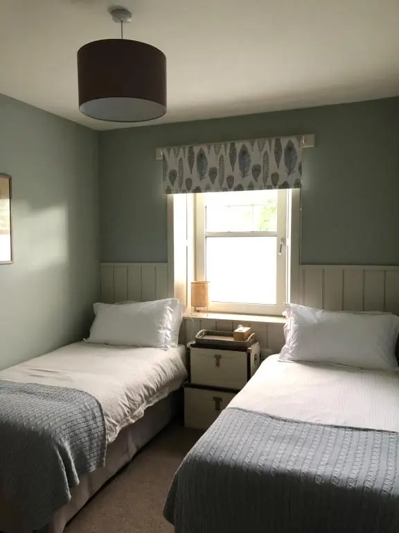 two beds in a room with a window and a window at Nurse's Cottage in Tomintoul