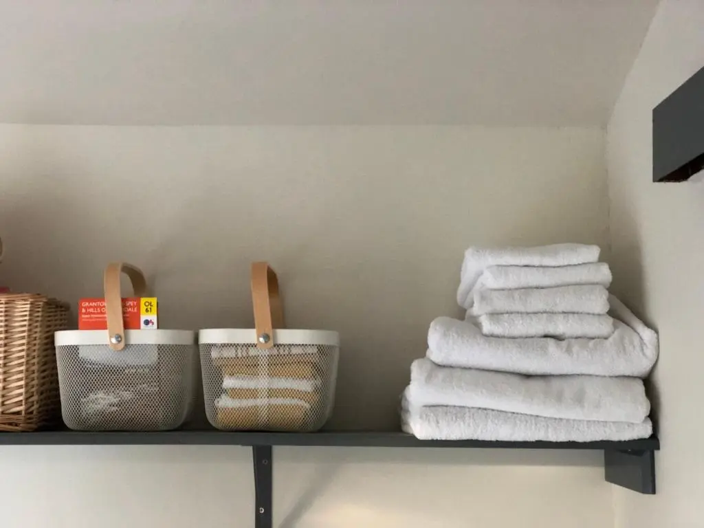 a shelf with towels and baskets on it in a bathroom at Nurse's Cottage in Tomintoul