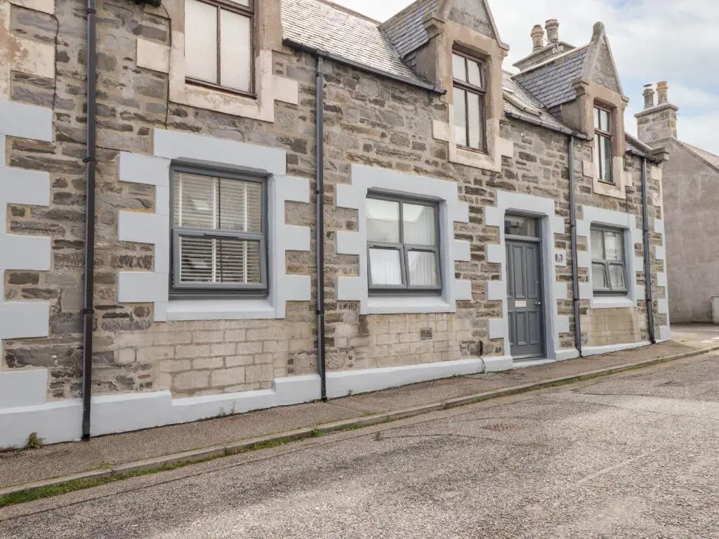 an old stone house with white windows on a street at 18b New Street in Buckie