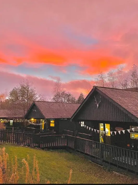 a barn with a fence in front of a sunset at Braemar Lodge Cabins Not for profit in Braemar