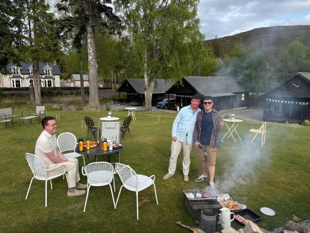 a group of three people standing around a fire at Braemar Lodge Cabins Not for profit in Braemar