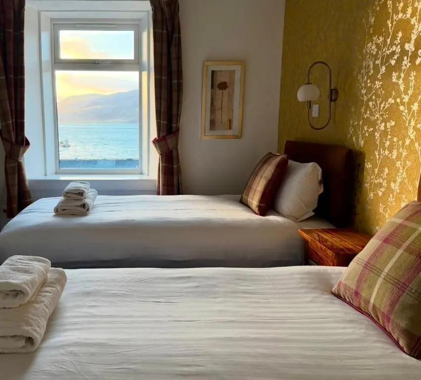 two beds in a hotel room with a window at The Ferry Boat Inn in Ullapool