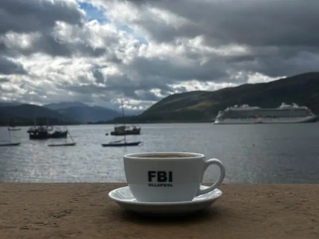 a cup of coffee sitting on a table near the water at The Ferry Boat Inn in Ullapool