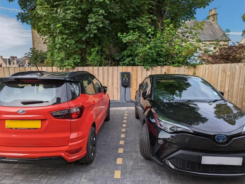 two cars parked in a parking lot next to a fence at The Ness Guest House in Inverness