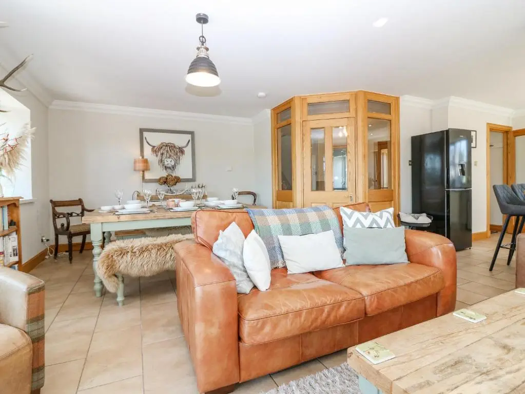 a living room with a brown couch and a kitchen at Stable Cottage in Inverurie