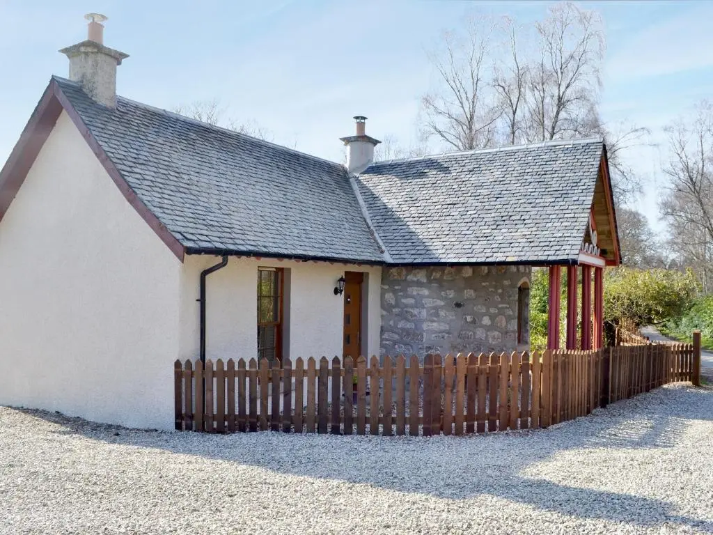 a small white cottage with a wooden fence at North Lodge Gate House in Urray
