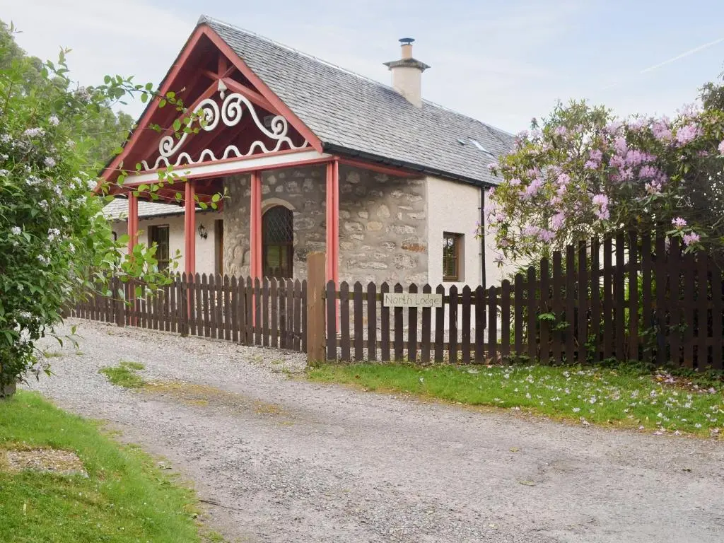 a small house with a wooden fence and flowers at North Lodge Gate House in Urray