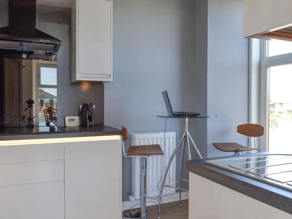 a kitchen with white cabinets and a counter with stools at Inver House Apartment in Inverurie