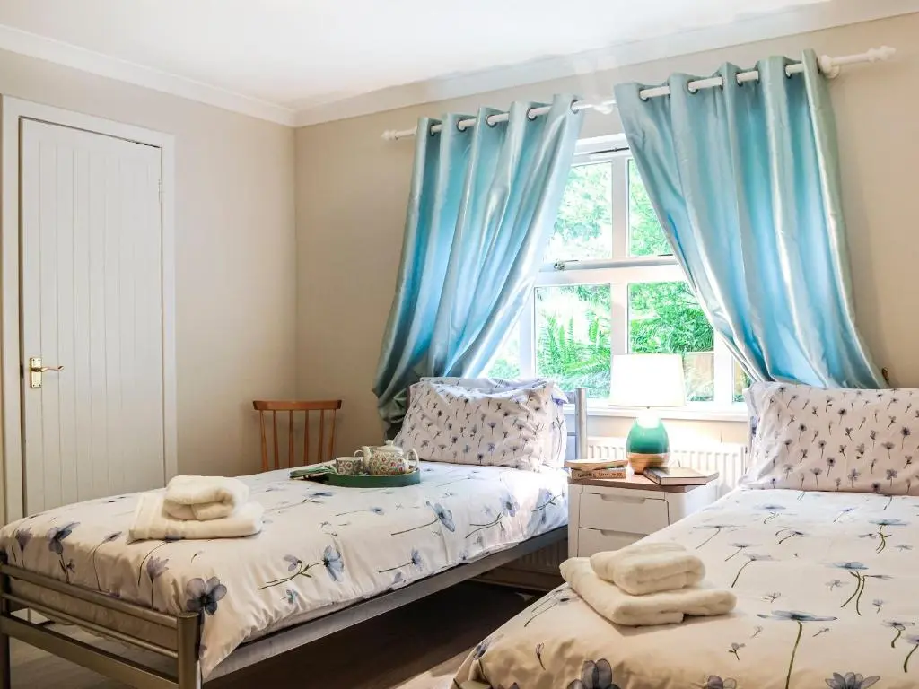 two beds in a bedroom with blue curtains at Corrennie School Cottage in Whitehouse