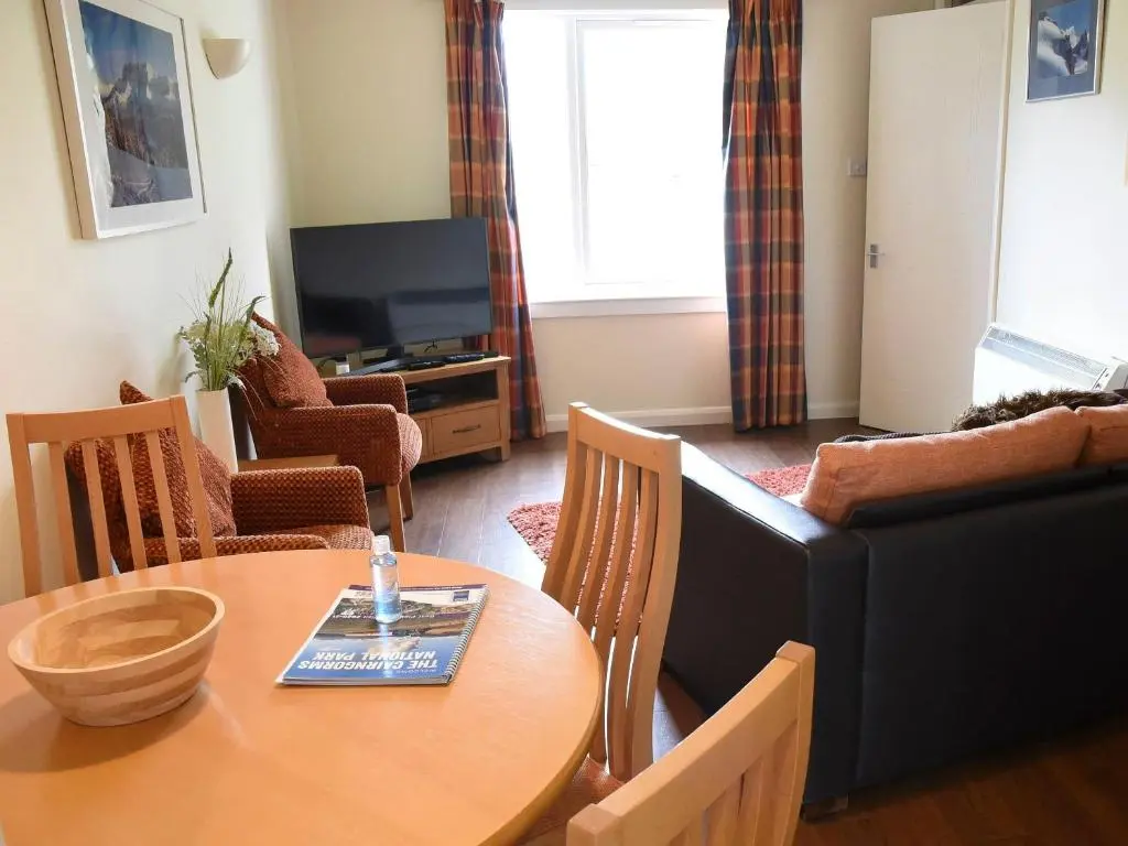 a living room with a table and a television at Bonnie Doon in Aviemore
