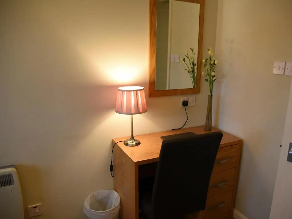 a desk with a lamp and a vase of flowers on it at Bonnie Doon in Aviemore
