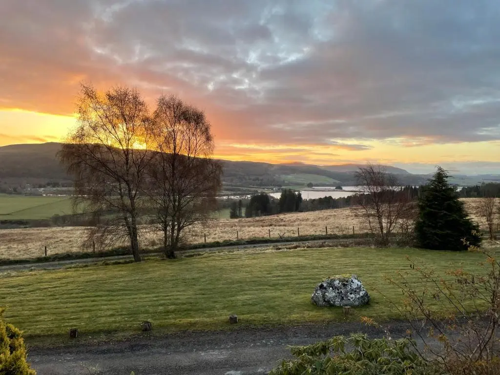 a field with a sunset in the background at Lower Hilton Cottage in Culrain
