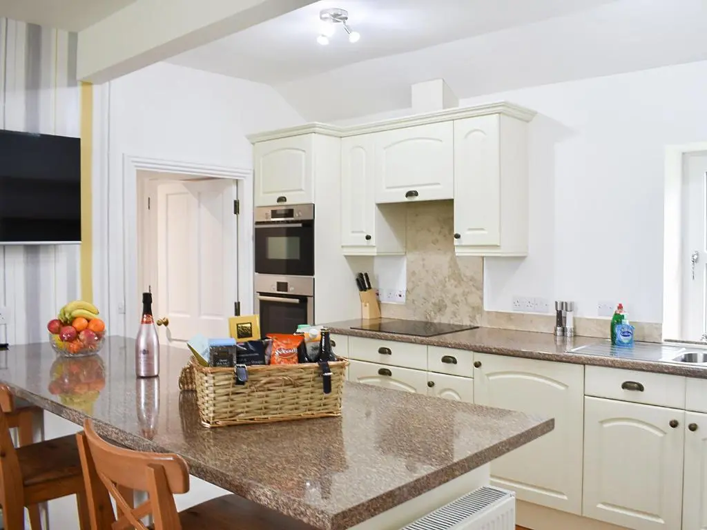 a kitchen with white cabinets and a table with a basket of fruit at 1 Dalbuaick Farm Cottage in Carrbridge