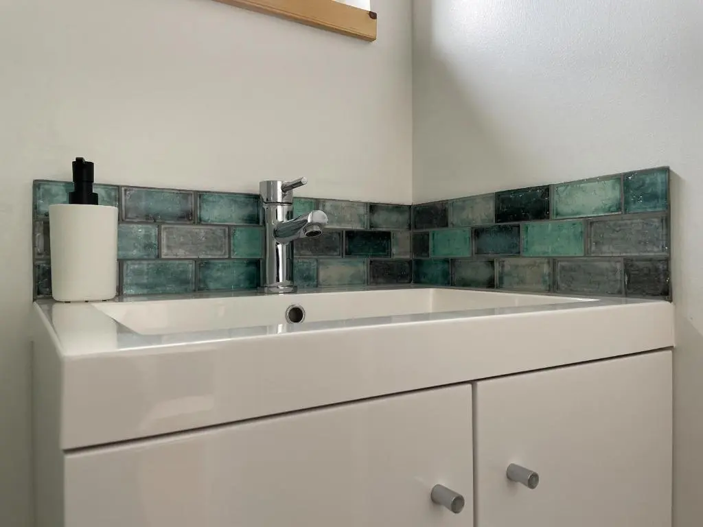 a white sink in a bathroom with green tiles at Sunrise Summerhouse in Hilton of Cadboll