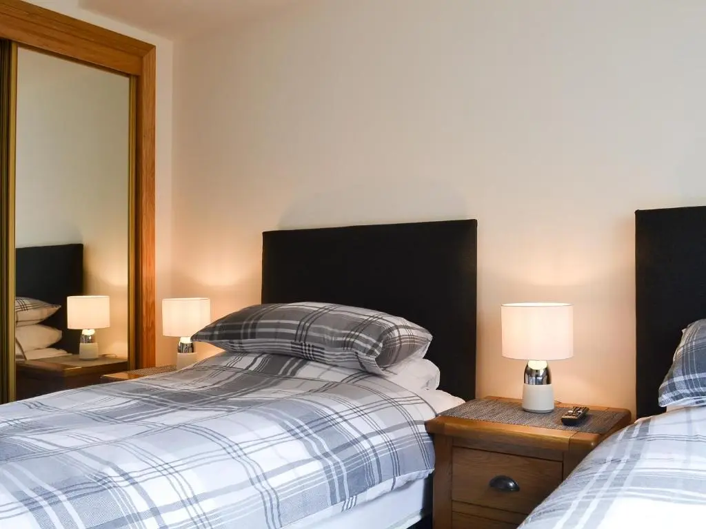 a bedroom with two beds and two lamps and a mirror at Aurora in Lossiemouth