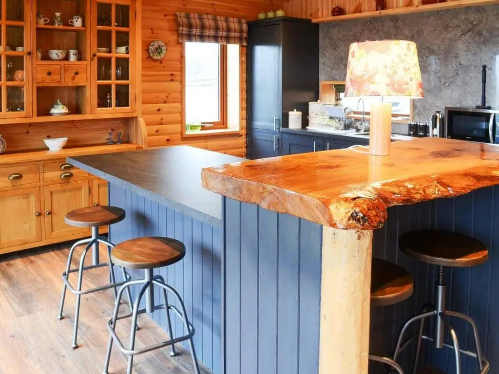 a kitchen with a blue island with bar stools at Red Kite & Osprey Lodges in Rhilochan