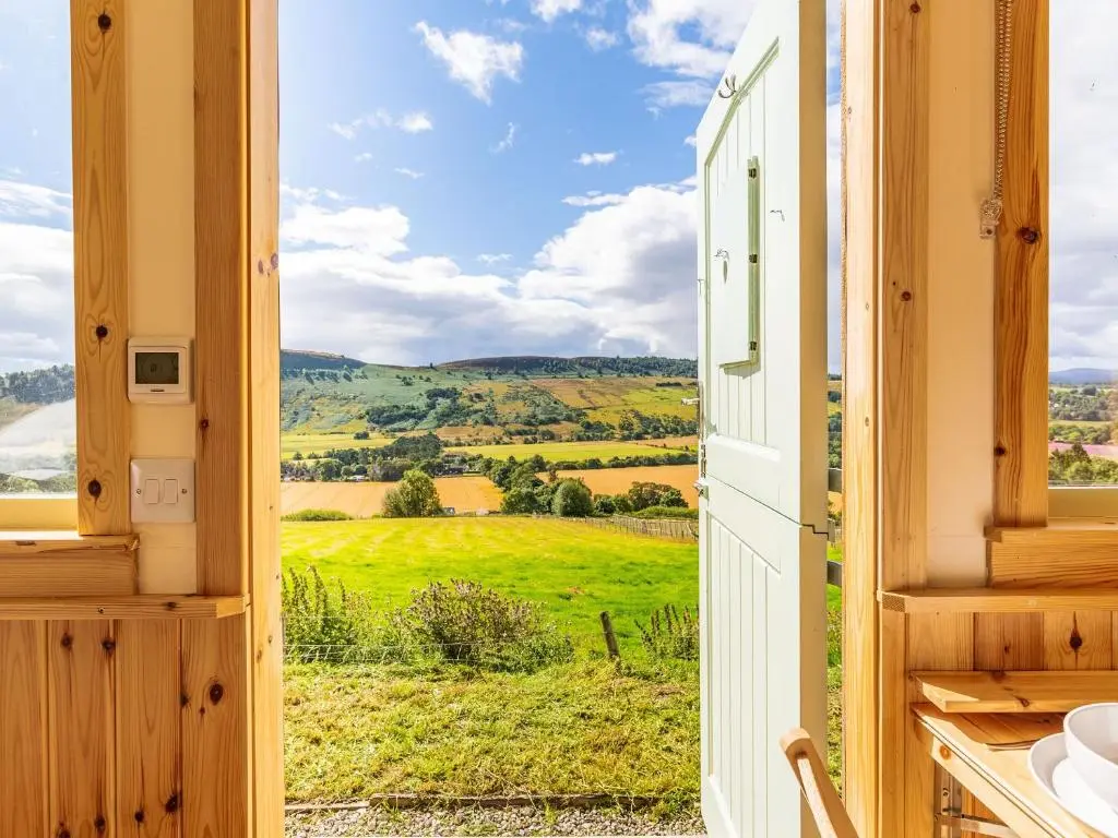 a room with a view of a green field through a door at Woodside Hut 2 - Uk36106 in Auchterneed