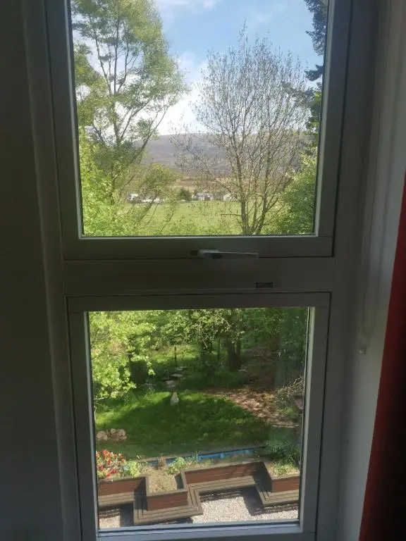 a window with a view of a garden at Dalwhinnie Old School Hostel in Dalwhinnie