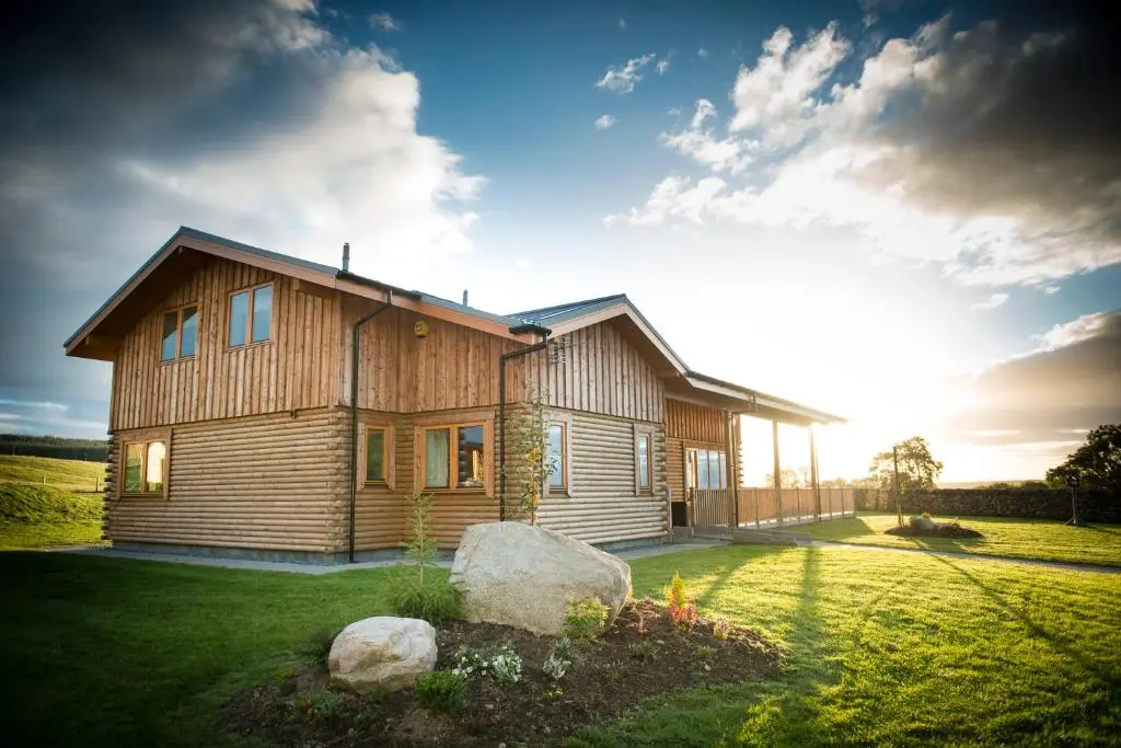 a wooden house in a field with the sun behind it at Blue Sky Lodges. Atlas & Aurae in Croy