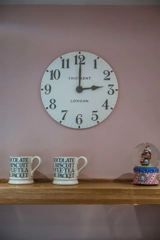 a clock on a wall above a shelf with two cups at Bramble Cottage in Turriff