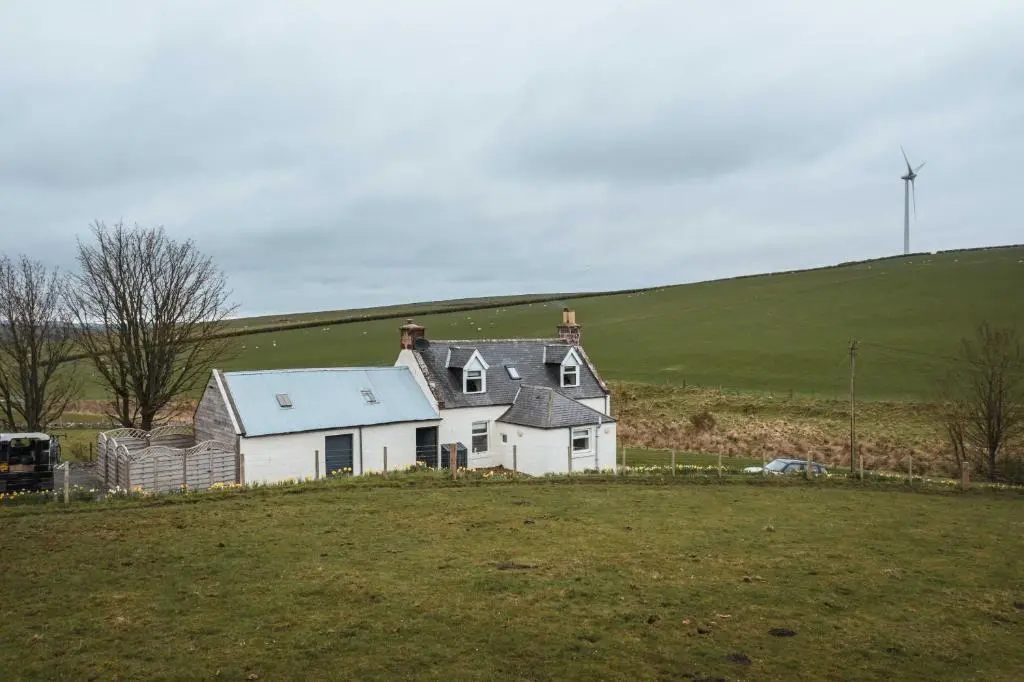 a white house in a field with a grass field at Bramble Cottage in Turriff
