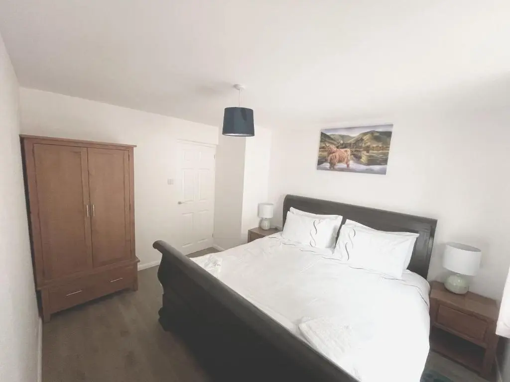 a bedroom with a bed with white sheets and a wooden cabinet at Matara House Holiday Home in Inverness
