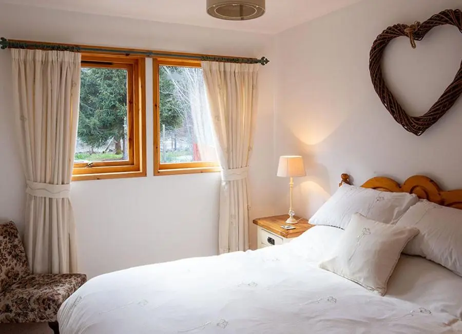 a bedroom with a white bed and a window at Croftwood Cottage in Boat of Garten