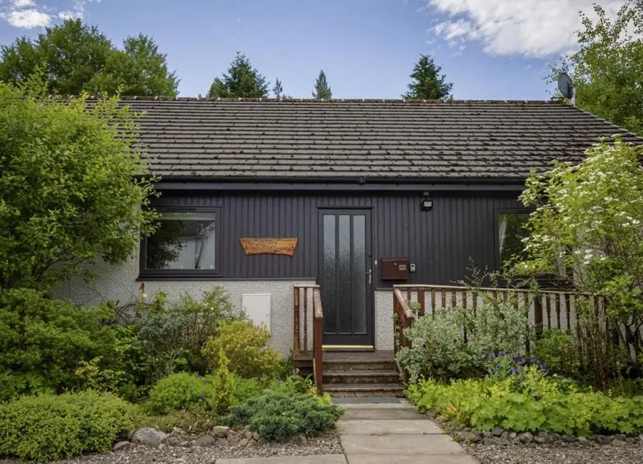 a small grey house with a door and stairs at Croftwood Cottage in Boat of Garten