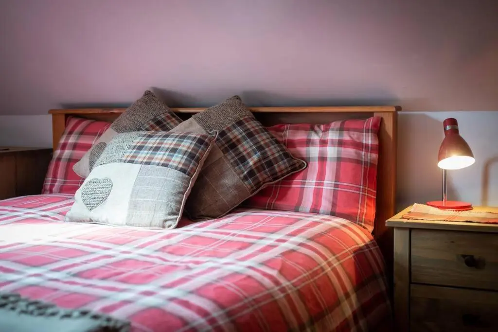 a bed with plaid pillows and a lamp on a table at The Beeches Studio, Highlands of Scotland in Newtonmore
