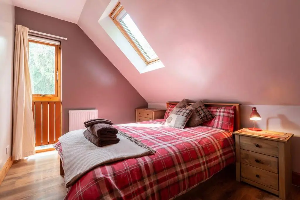 a bedroom with a bed with a red blanket and a window at The Beeches Studio, Highlands of Scotland in Newtonmore