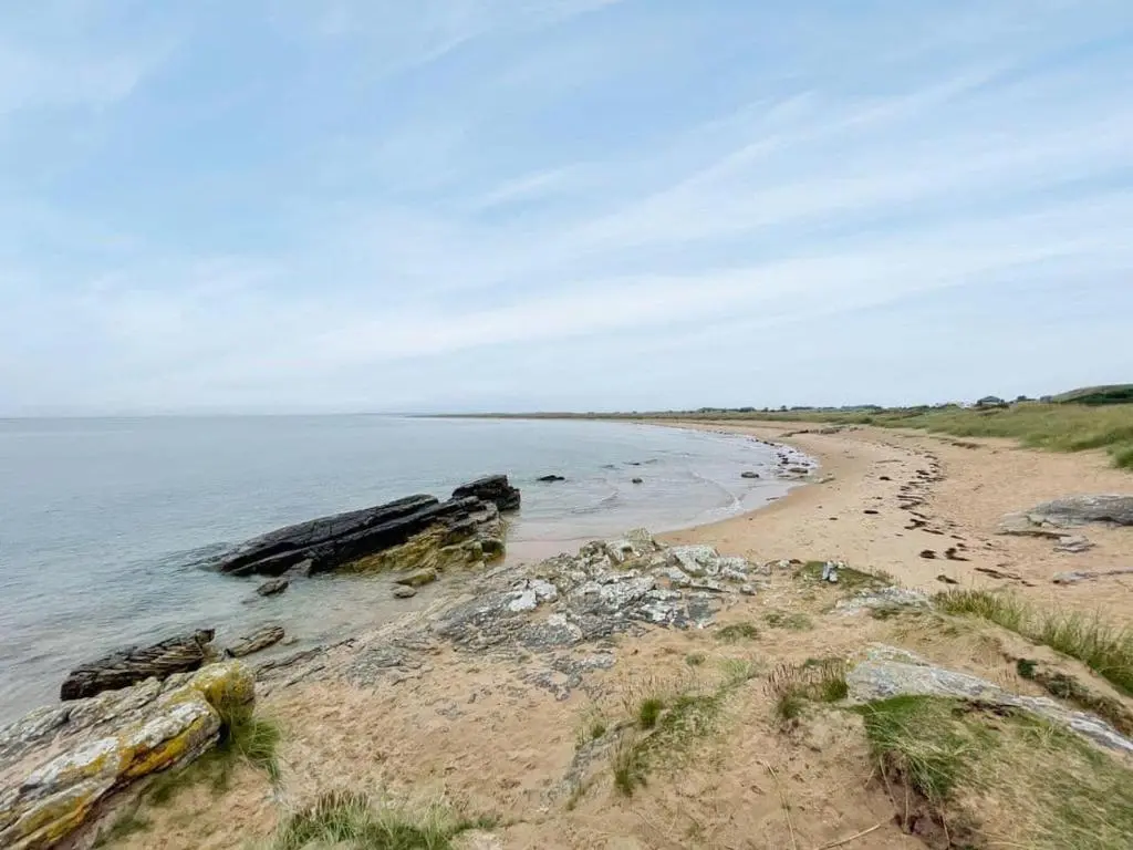 a sandy beach with rocks and the ocean at Balloan Steading West in Dornoch