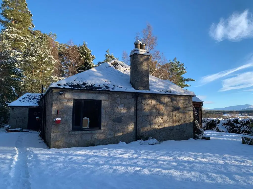 a small stone building with a chimney in the snow at Wester Curr Cottage - Luxury 5-Star Cottage with Private Pool & Hot Tub in Grantown on Spey