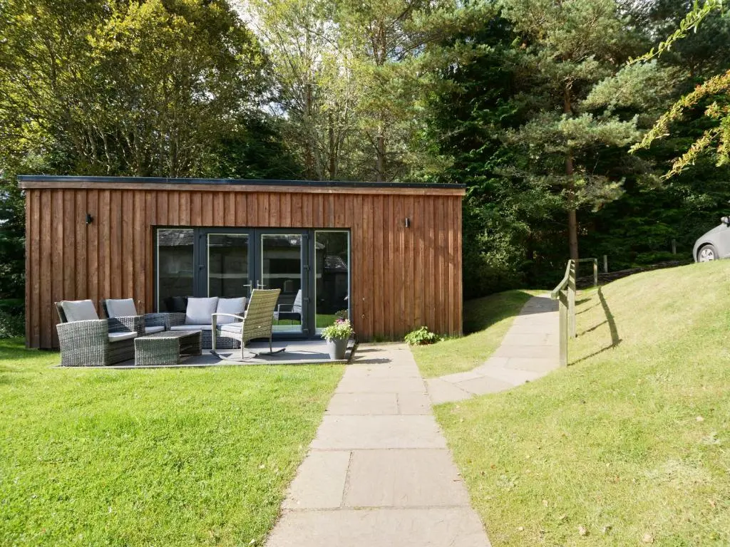 a shed with a patio and chairs in a yard at Wester Curr Cottage - Luxury 5-Star Cottage with Private Pool & Hot Tub in Grantown on Spey