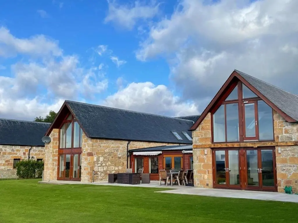 a large stone building with windows and a lawn at Balloan Steading East in Dornoch