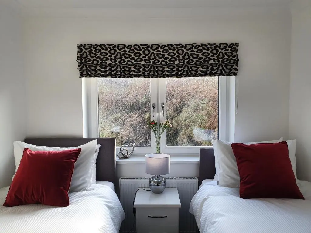 a bedroom with two beds and a window with a window shade at 22 Waters Edge Banff in Banff