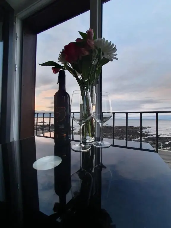 a table with a bottle and two glasses and flowers at 22 Waters Edge Banff in Banff