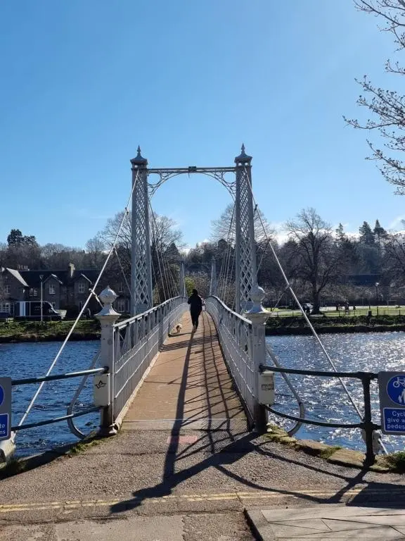 a person walking across a bridge over a body of water at The 'Fairy Hill' Apartment in Inverness