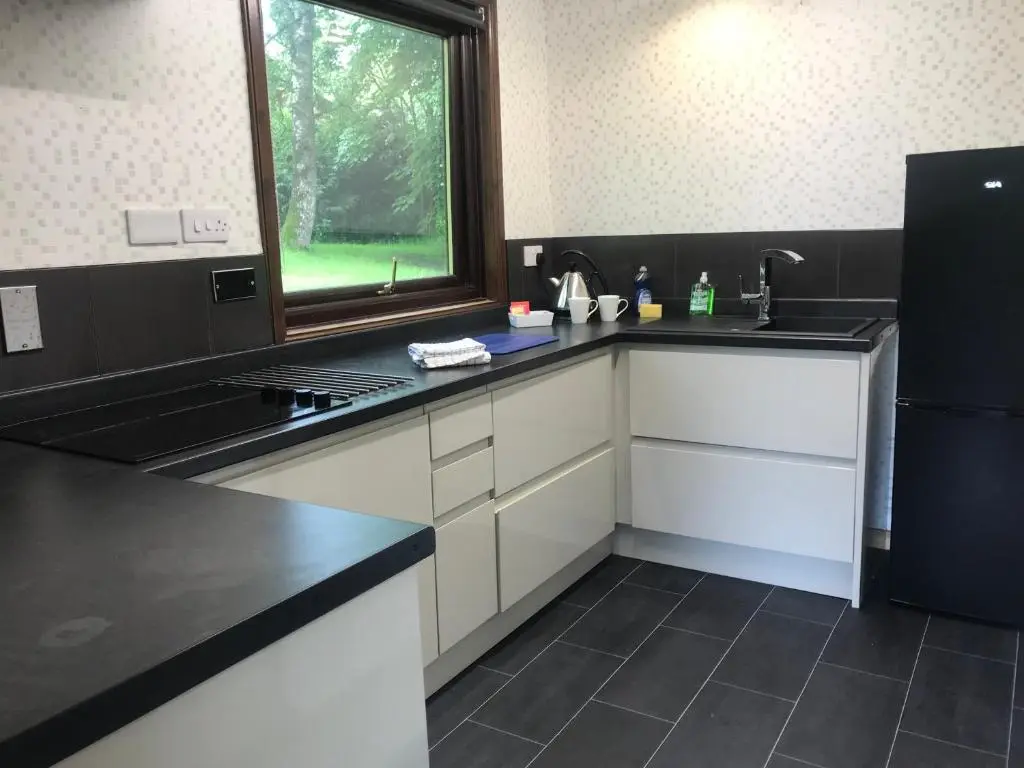 a kitchen with white cabinets and a black counter top at Pine Chalet in Muir of Ord
