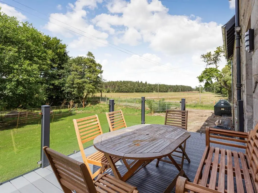 a wooden table and chairs on a patio with a field at New Cottage in Farr