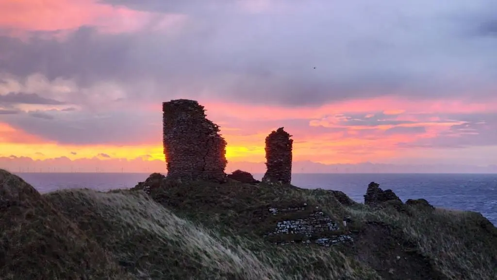a group of ruins on a hill with a sunset at Castle Shieling in Latheron
