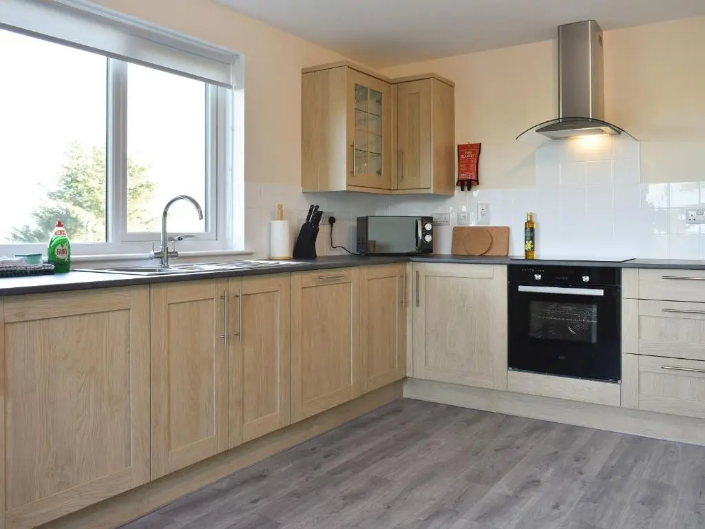 a kitchen with wooden cabinets and a black appliance at Benwells Holiday Cottage in Maud