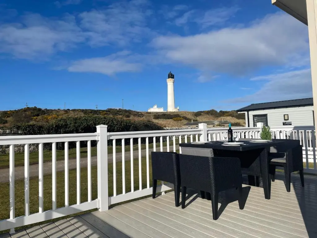 a wooden deck with a lighthouse in the background at The Hudson @ Silversands in Lossiemouth