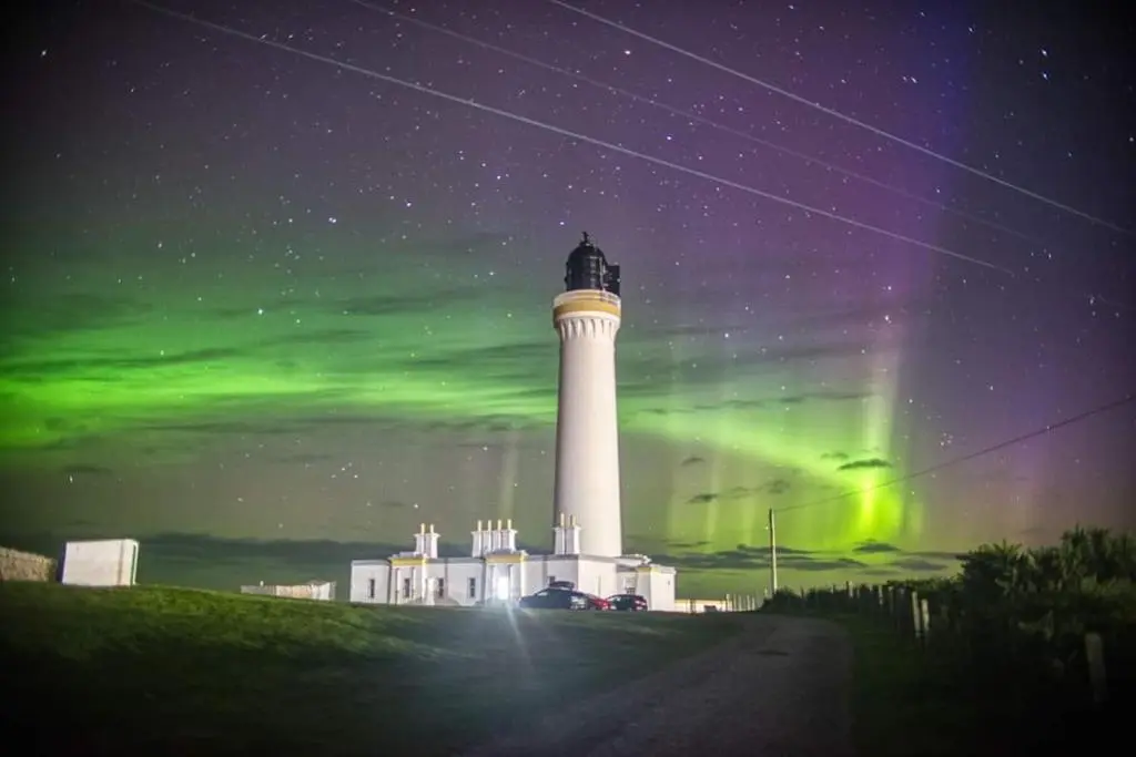 a lighthouse under the northern lights with a green sky at The Hudson @ Silversands in Lossiemouth