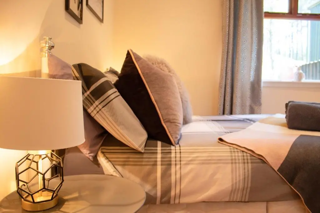a bedroom with a bed with pillows and a lamp at Druim An Lochain Cottage in Kinrara