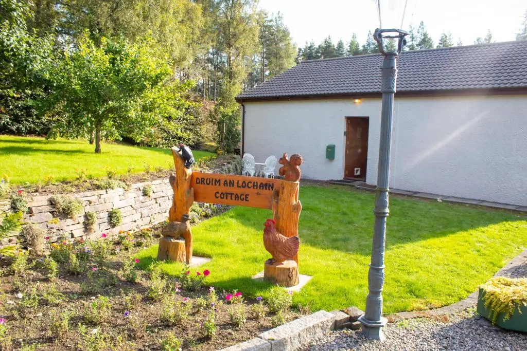 a sign in a yard next to a house at Druim An Lochain Cottage in Kinrara