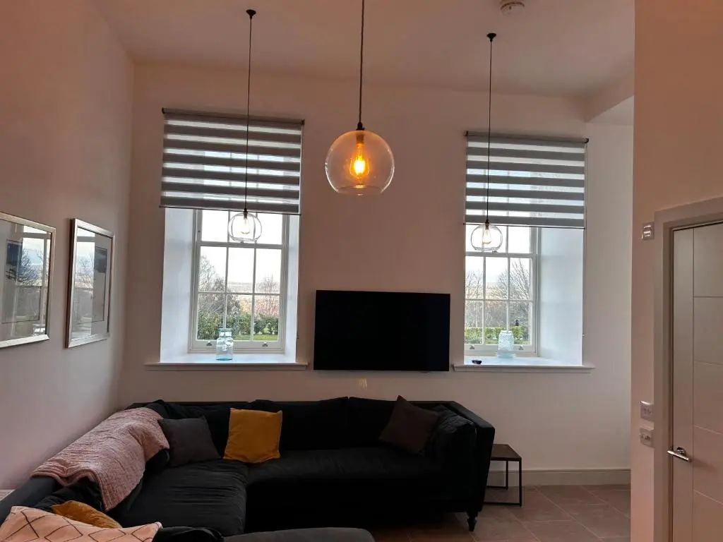 a living room with a black couch and two windows at 38 Great Glen Townhouse Inverness in Inverness