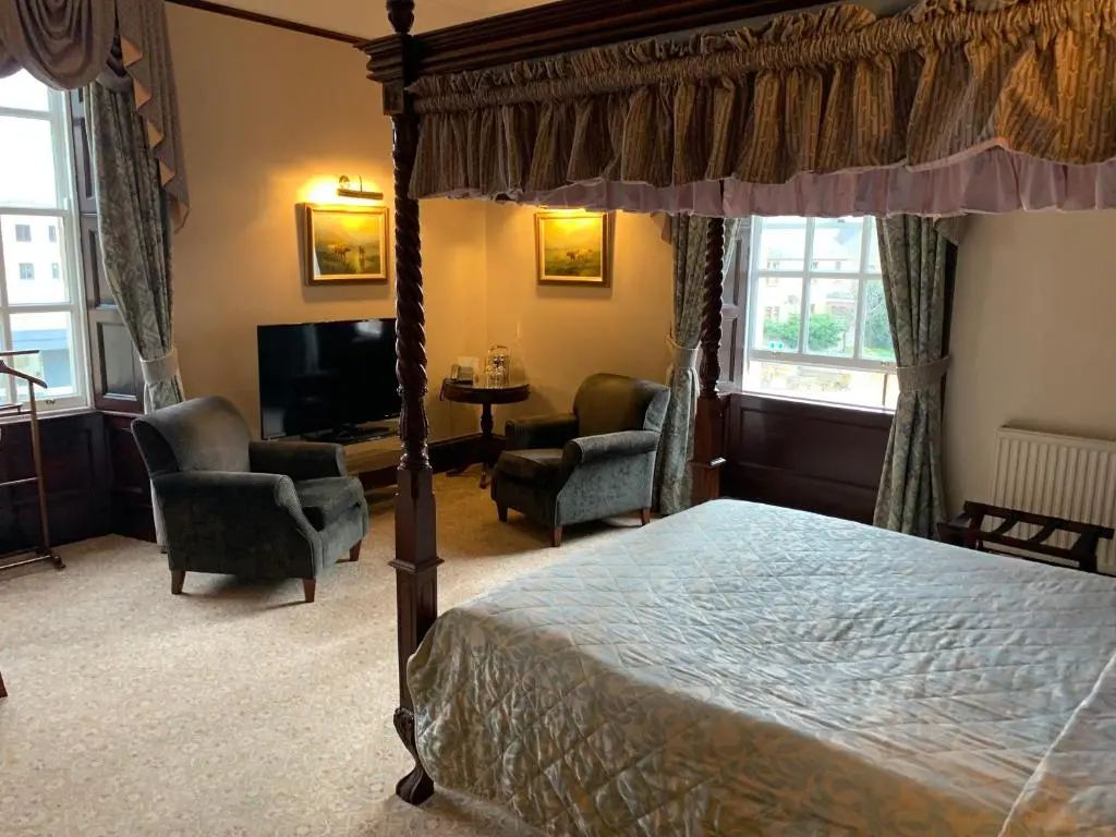 a bedroom with a canopy bed and chairs and a television at The Mansefield Hotel in Elgin