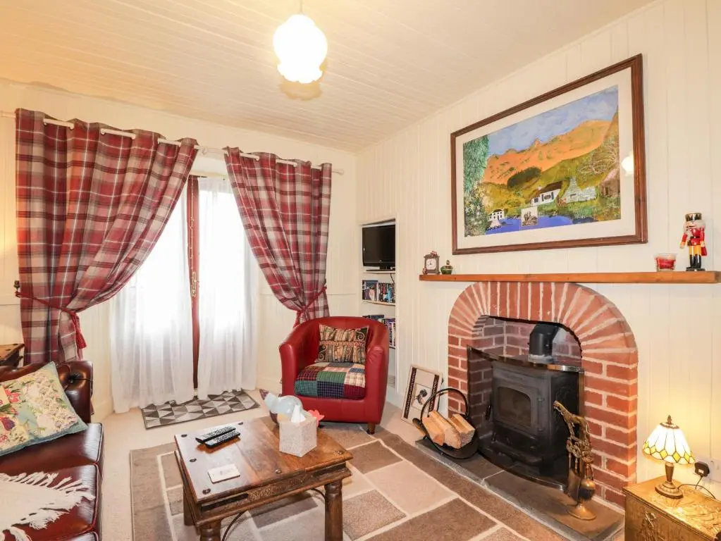 a living room with a fireplace and a red chair at Bogindour Cottage in Muir of Ord