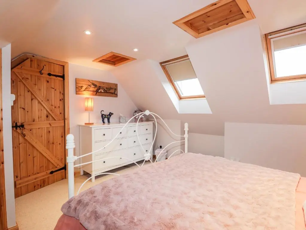 a attic bedroom with a white bed and windows at Bogindour Cottage in Muir of Ord