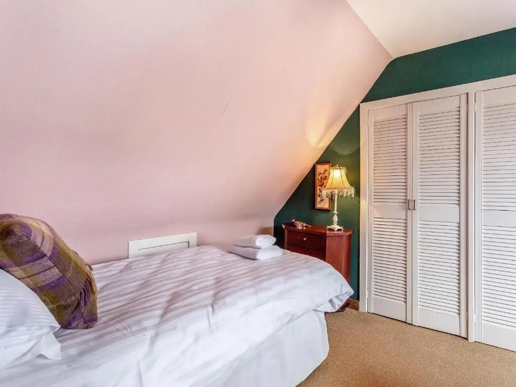 a bedroom with a white bed and a green wall at Holly Tree Cottage in Tain